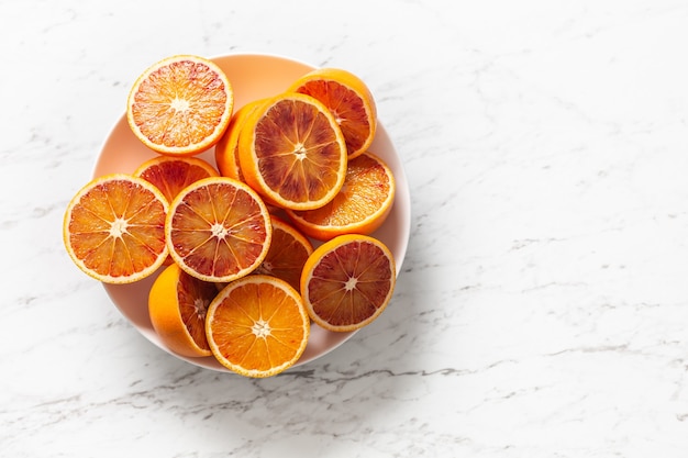 Sliced red oranges in a plate on a marble white table - top of view.