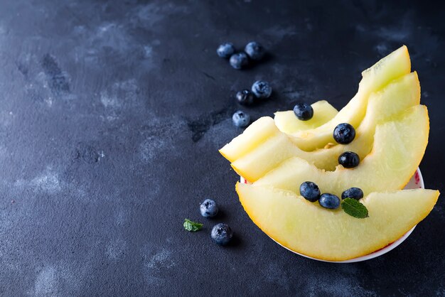 Sliced ripe melon on a plate on a dark stone background