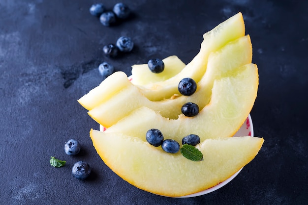 Sliced ripe melon on a plate on a dark stone background