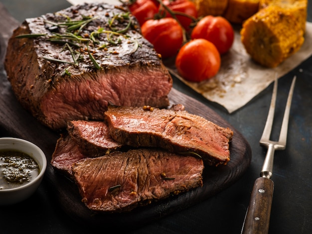 Sliced Roast beef on cutting board with grilled vegetables.