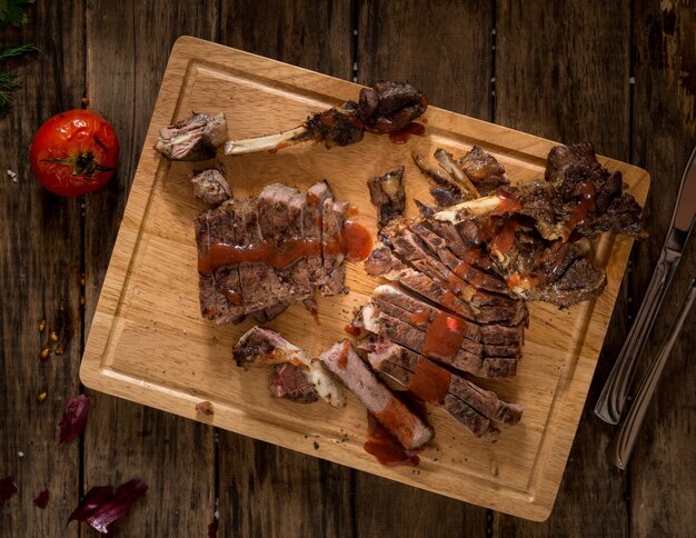 Sliced roasted meat on a wooden surface and dressed with sauce, top view