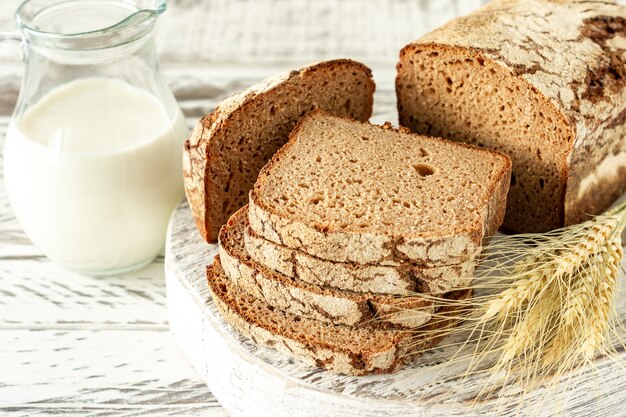 Sliced rye bread on wooden cutting board next to jug with milk. Tasty food close up. Homemade baked bread.