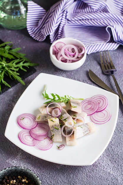 Sliced salted herring in oil with onion and dill on a plate Simple snack Vertical view