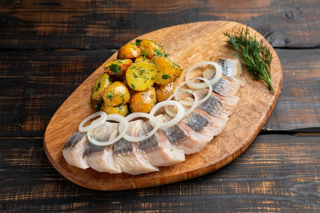 Photo sliced salted herring with baked potato, onion and dill on cutting board rustic style