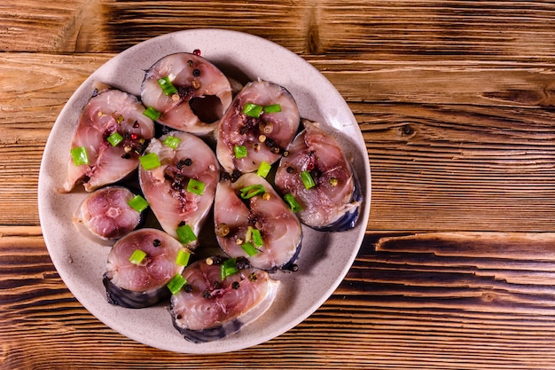 Sliced scomber fish with green onion on a ceramic plate on rustic wooden table. Top view