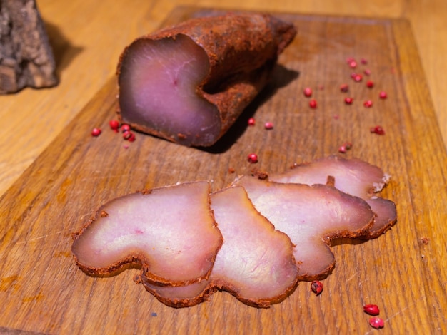Sliced smoked gammon on a wooden table with addition of fresh herbs and aromatic spices
