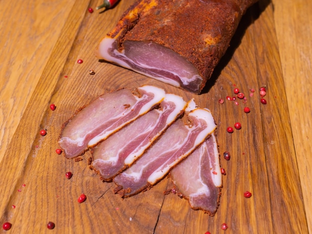 Sliced smoked gammon on a wooden table with addition of fresh herbs and aromatic spices