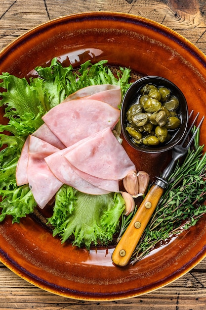 Sliced smoked ham with fresh salad and capers on a plate. wooden background. Top view.