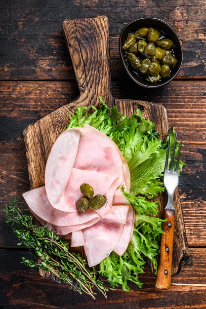 Sliced smoked ham with fresh salad and herbs on wooden table. Top view.