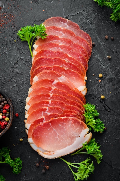 Sliced smoked meat with spices and herbs On a black wooden background Top view Free space for your text