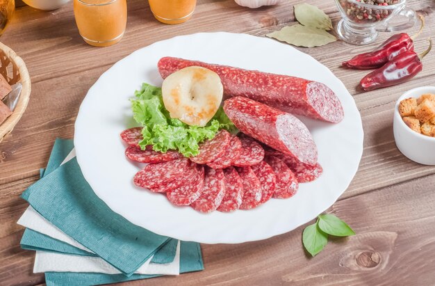 Sliced smoked sausage with lard on a white plate on a dark wooden background.