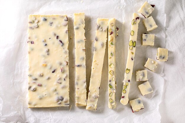 Sliced strips and squares homemade white chocolate candy bar with pistachios nuts and cranberries on crumpled paper. Handmade food sweet gifts for any holidays.