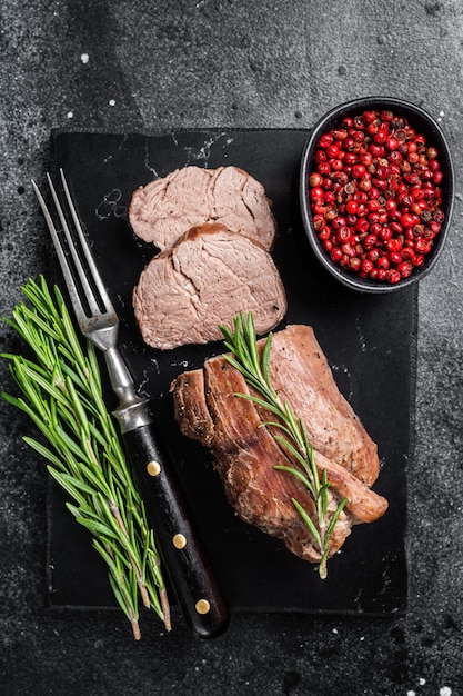 Sliced tenderloin Steak Roast beef on marble board with rosemary Black background Top view