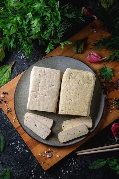 Sliced tofu soy cheese on a cutting board with basil spices and vegetables