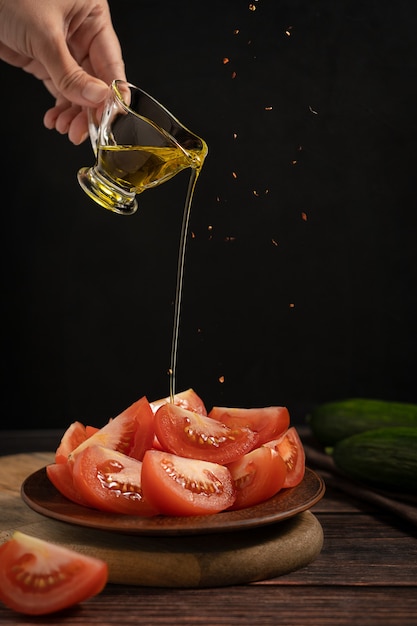 Sliced tomato vegetable served on plate with hand pouring olive oil and spice falling on table