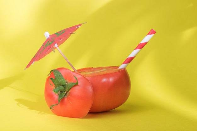 Sliced tomato with a cocktail umbrella and a straw in the shade of tropical plants. The concept of consumption of fresh vegetable juice.