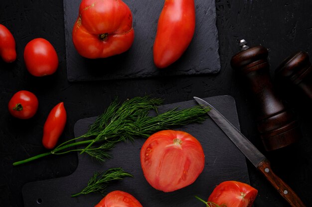 Foto pomodori a fette su un aneto di ardesia verdi due mulini per spezie e coltello con manico in legno su sfondo scuro