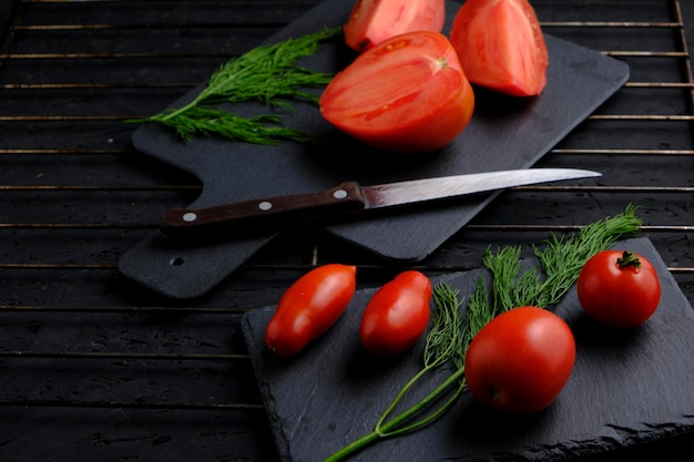Sliced tomatoes on slate dill and knife with wooden handle on grill