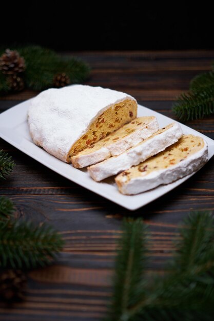 Sliced traditional christmas stollen cake with marzipan and dried fruit on wooden background