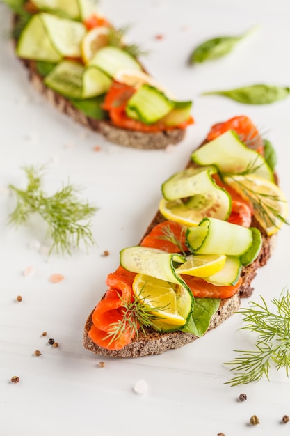 Trota affettata (salmone) sandwich di pesce con ogerets, pane di segale e aneto su sfondo bianco.