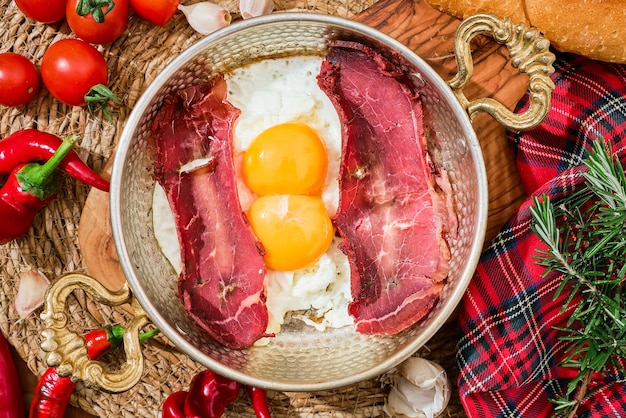 Sliced Turkish bacon pastrima for breakfast fried beef with eggs peppers and vegetables in a traditional copper Turkish pan top view local cuisine