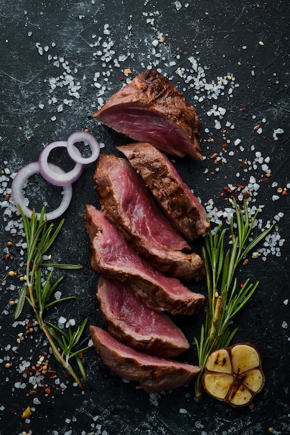 Sliced veal juicy steak on black stone background Top view Free copy space