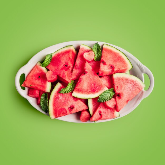 Нарезанные ягоды арбуза, свежие фрукты на тарелке. Одиночный объект, изолированные на зеленом фоне. Вид сверху, плоская планировка