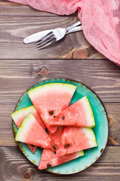 Sliced watermelon on a ceramic plate, cutlery and napkin on woodtable Top view