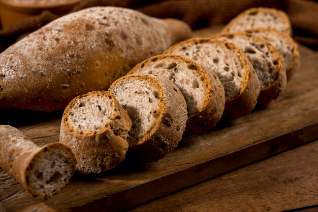Sliced whole grain bread, baguettes on rustic wood with whole\
flour pot in the background.