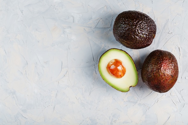 Sliced and whole organic Hass avocado on a gray surface