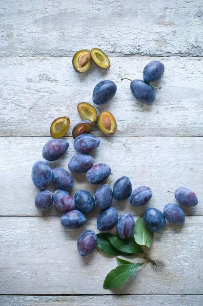 Sliced and whole plums on white wood