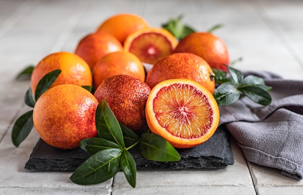 Sliced and whole ripe juicy sicilian blood oranges with leaves\
on black board seasonal fruits