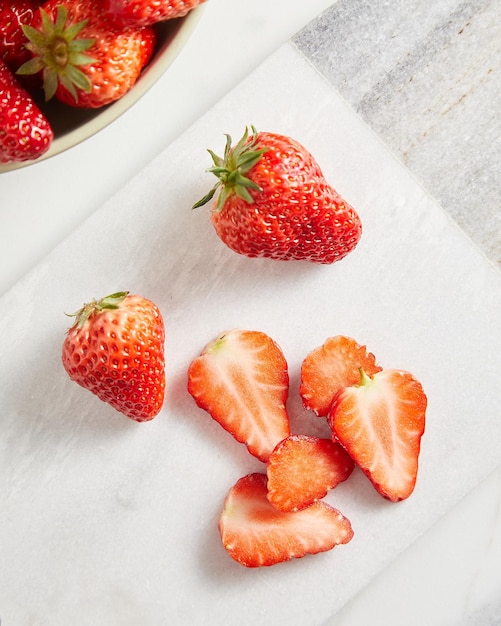 Sliced and whole strawberries on white cutting board