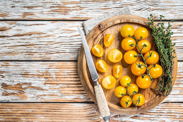 Sliced yellow cherry tomato on a wooden tray with herbs. White wooden background. Top view. Copy space.