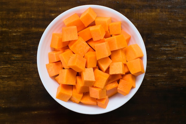 Slices of autumn pumpkins in a white plate on a wooden background. Top view.