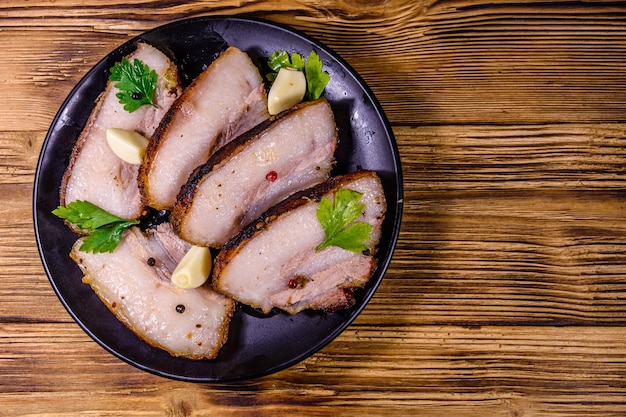 Slices of baked pork belly, garlic and parsley on a black plate. Top view