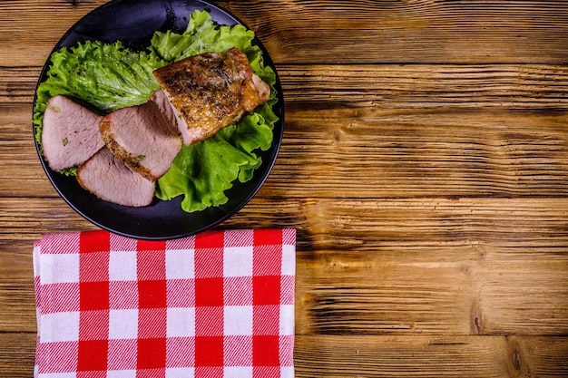 Foto fette di carne di maiale al forno e foglie di lattuga su un piatto nero. vista dall'alto