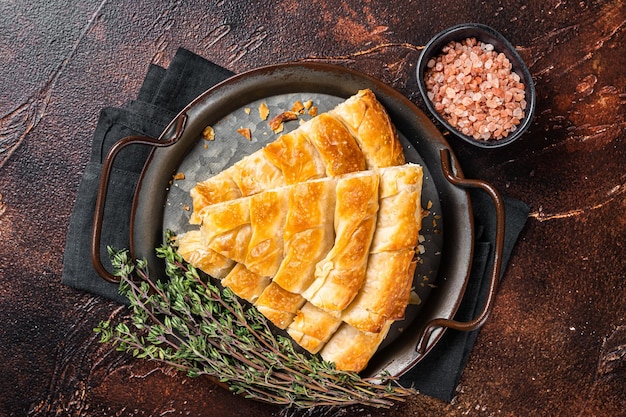 Slices of baked Round Borek cheese pie in kitchen tray with herbs Dark background Top view