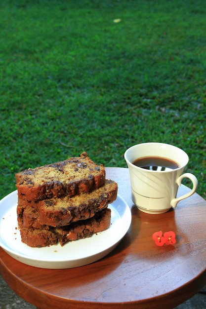 白い皿にバナナブレッドのスライスと庭での朝食のためのコーヒーのカップ