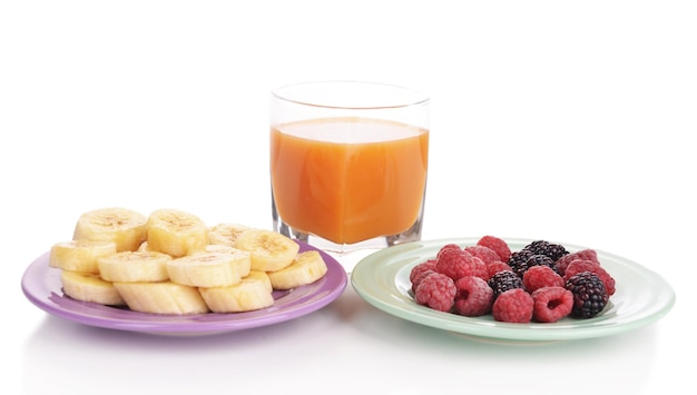 Slices of bananas with berries on plate with glass of juice isolated on white