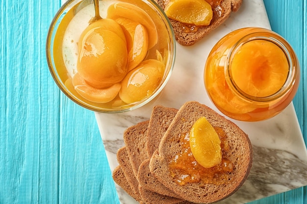 Slices of bread bowl and jar with pickled apricots on table