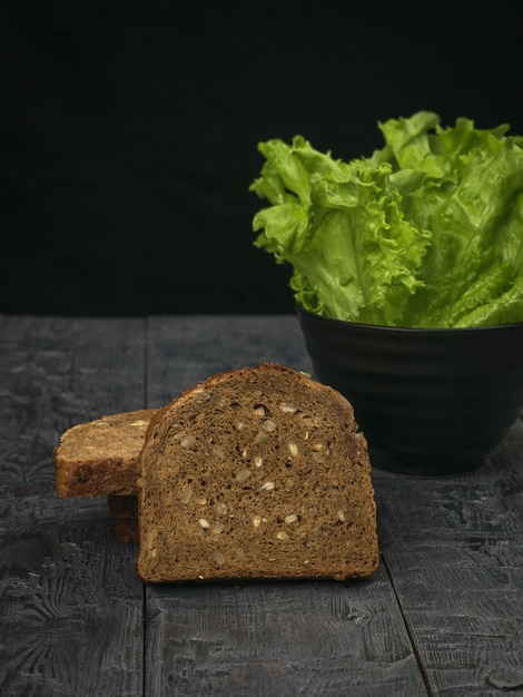 Ломтики хлеба с цельным зерном и миска с листьями салата на деревянном столе. Здоровое питание.