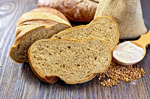 Slices of buckwheat bread, a bag of groats and flour in a spoon on a wooden boards background