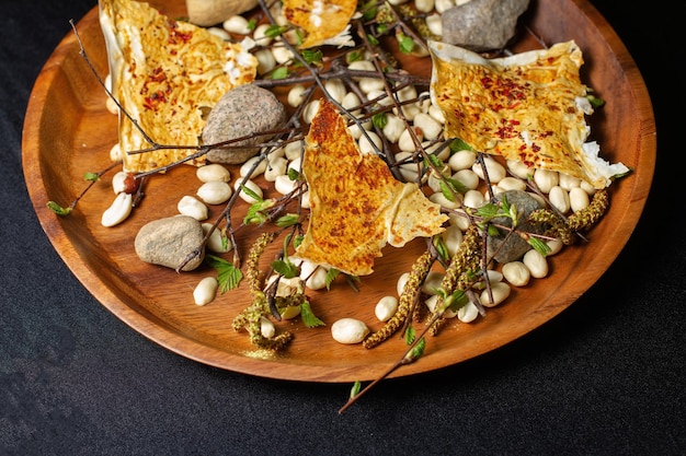 Slices of cakes with spices are laid out on a wooden platter decorated with peanuts stones and twigs
