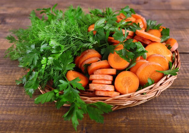 Slices of carrot and parsley in wicker bowl on wooden background