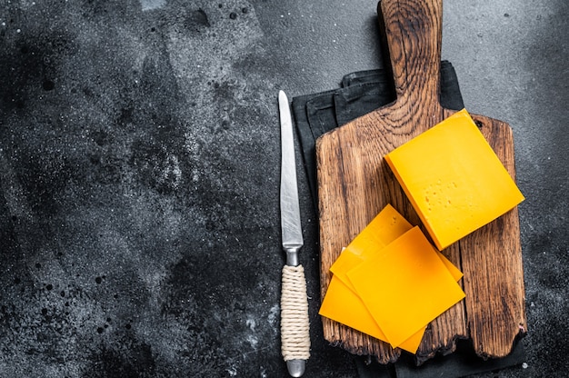 Photo slices of cheddar cheese on a wooden cutting board. black background. top view. copy space.