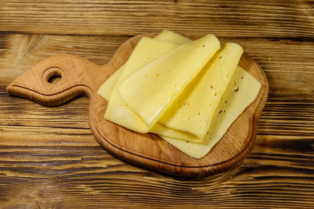 Slices of cheese on cutting board on wooden table