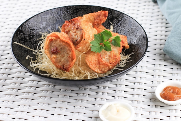 Slices of Chicken Egg Rolls, is Omelete Egg Stuffed with Ground Chicken and Spices, Steamed and Deep Fry, Served with Chili Mayonaise Sauce Above Crispy Vermicelli