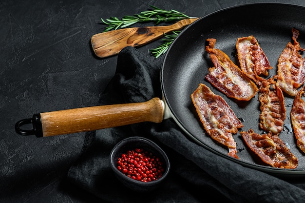 Slices of crispy hot fried cooked bacon. Farm organic meat. Black background. Top view