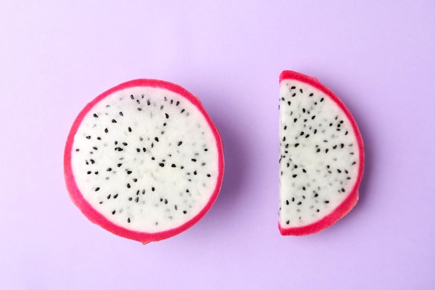 Slices of delicious dragon fruit pitahaya on violet background flat lay